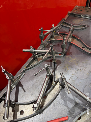 A ridiculous number of clamps are holding various points on the frame and tentacles to the table while two clamps hold down a cross-bracing piece of angle iron between two tentacles